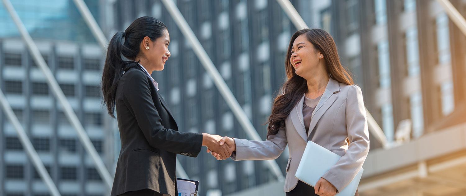 Two women shake hand in front of office building